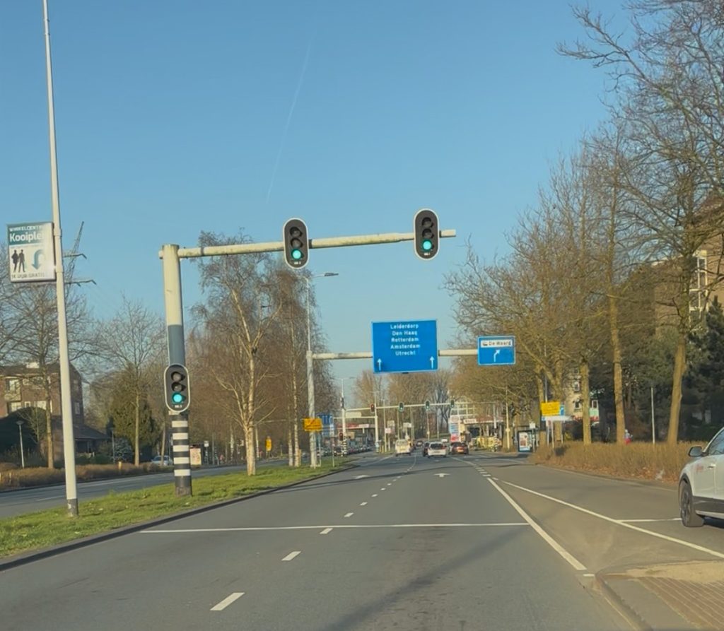 Een afbeelding van de Willem de Zwijgerlaan vanuit een auto genomen. Er staan meerdere verkeerslichten achter elkaar op groen.